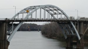 Schoolnik visiting the Edmund Pettus Bridge Selma, Alabama. Metal bridge over river on grey day.