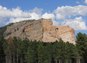 Crazy Horse Custer South Dakota. Giant mountain carving, with blue skies overhead and pine trees in foreground.