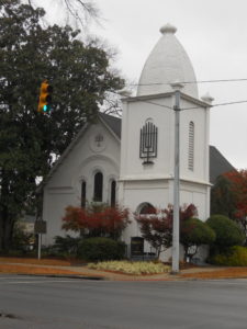 Southern Synagogues: Temple Beth El Anniston Alabama. White building on street corner with menorah sculpture above front door.