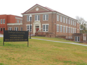 Schoolnik visiting the Tuskegee University National Center for Bioethics in Research and Health Care Tuskegee Alabama. Rectangular brick building with adjacent lawn.